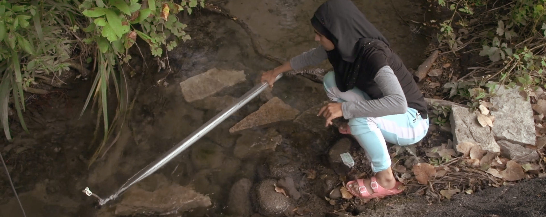 A student uses a tool to test water in a creek.
