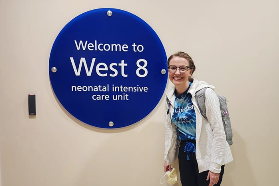Keeley O'Dell poses by a sign that says Welcome to West 8 neonatal intensive care unit.