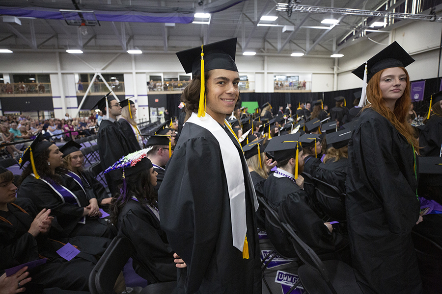 A student wearing their cap and gown smiles at the camera during graduation.