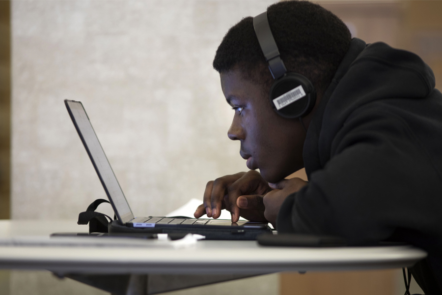 A student works on a laptop while wearing headphones.
