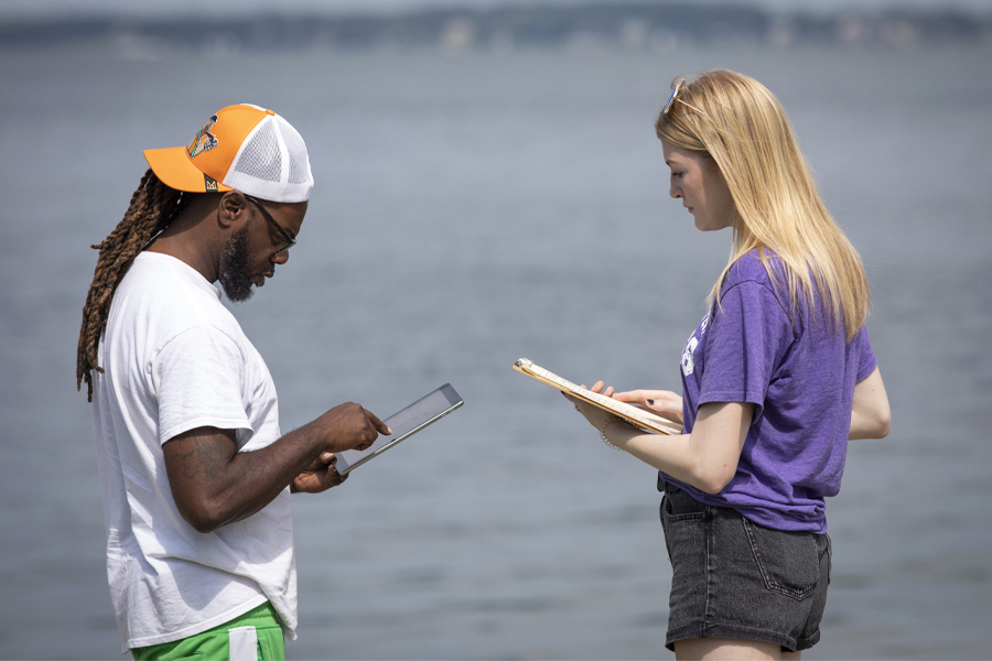 Two people talk while holding folders and a tablet.