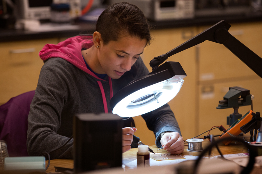 A student solders groups of micro wires under a large light.