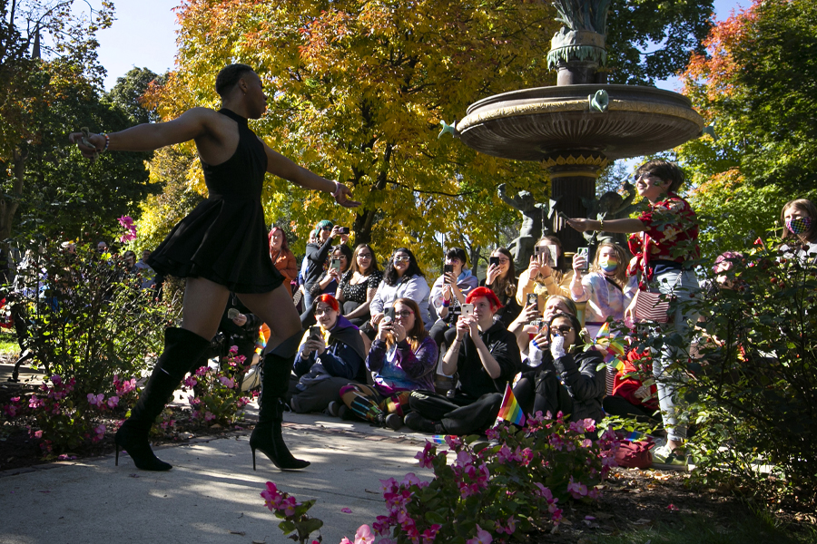 A person dances in front of a crowd by a fountain with fall trees in the background.