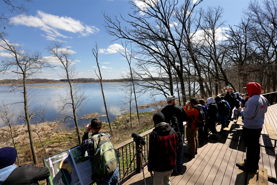 Biology majors stand on a deck overlooking a body of water.