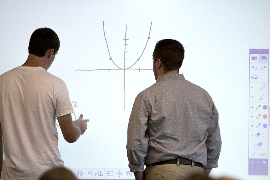 Two people at a white board drawing a graph.