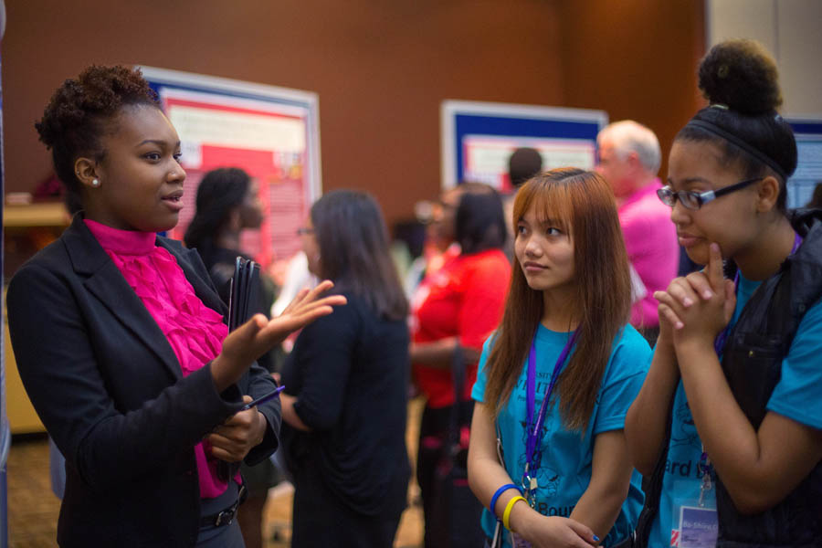 Three students talk with research posters in the background.
