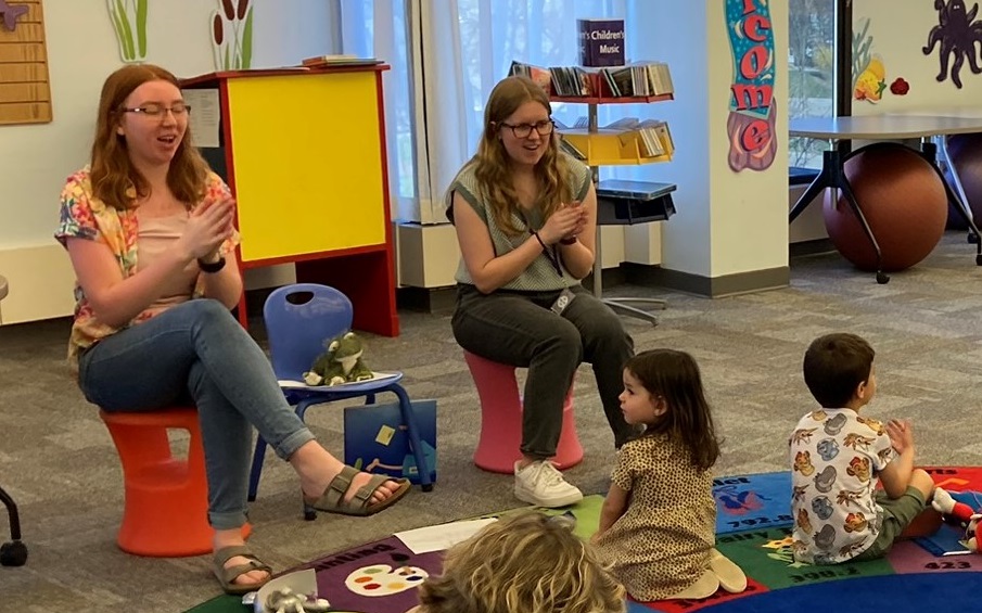 Two College of Education students reading to children and stuffed animals