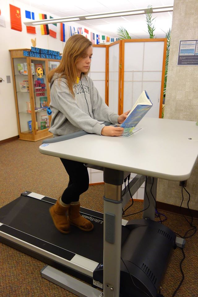 Student reading while using the treadmill desk at Andersen Library