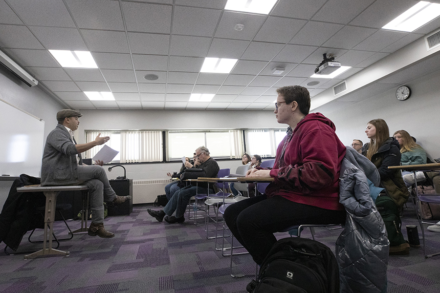 Nicholas Gulig sits on a table at the front of class and speaks to his students.