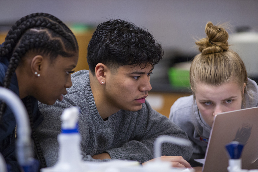 Three students work together on a laptop.