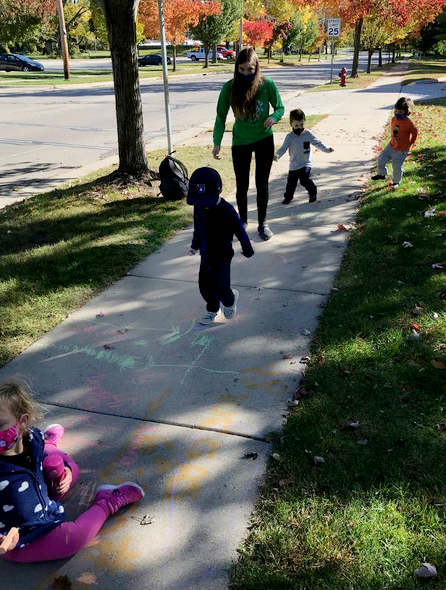 Student with children chalking on a sidewalk.