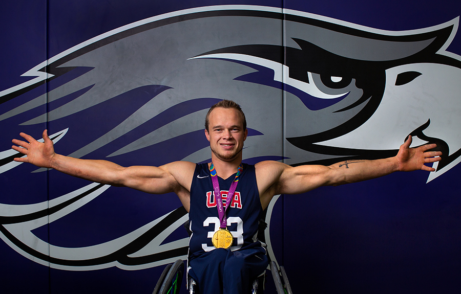 John Boie, member of Team USA, is in front of a Warhawk wall with his arms spread. 