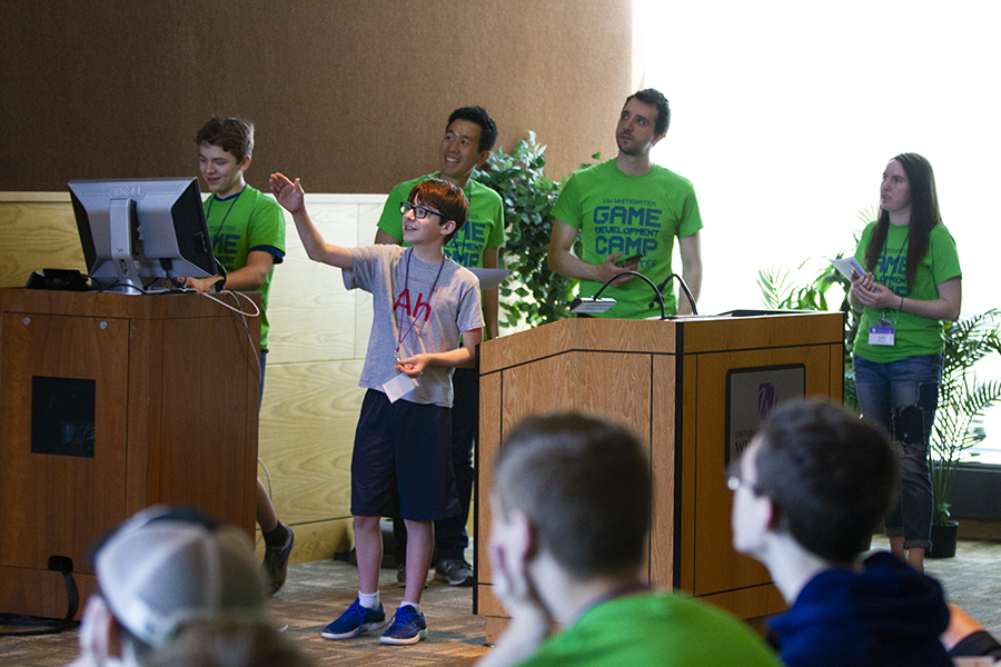 Young people gathered around a podium at an electronic game development camp.