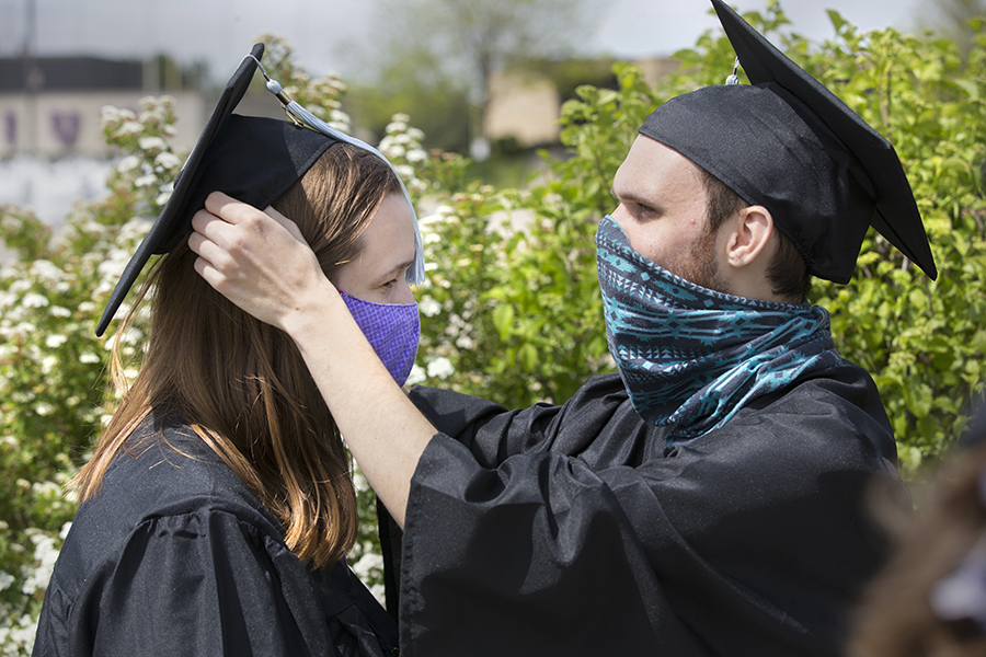 One students helps another student with their graduation cap.