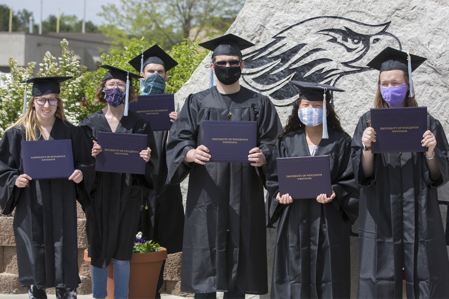 Six Warhawks stand outside wearing caps and gowns.