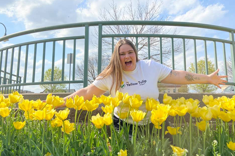 Kelsey Pacetti stands with her arms out in a field of yellow tulips.