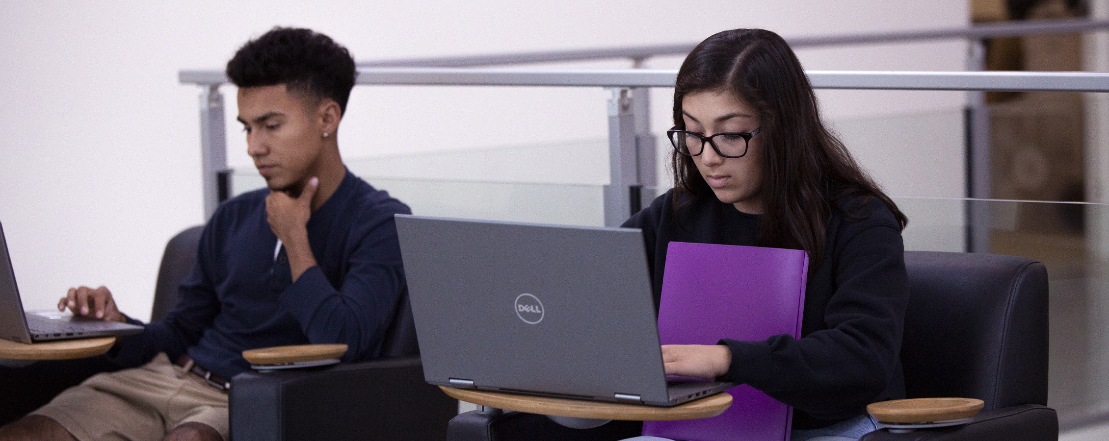 Dos estudiantes que trabajan con computadoras portátiles en un área de reunión.