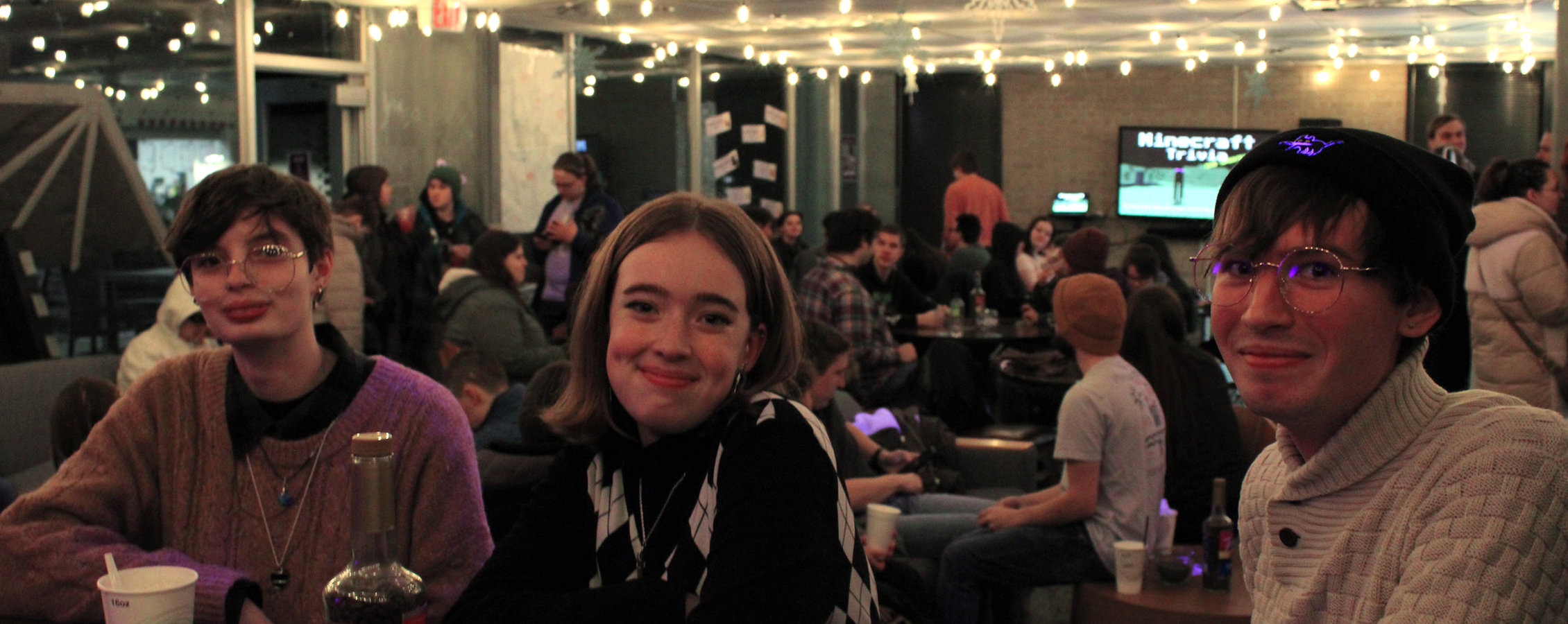 Three students sit together in Jitters which is full of people and lit by small white lights strung on the ceiling.