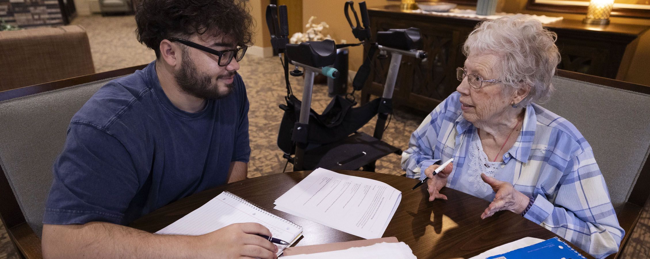 A senior citizen talks to a student at a table.
