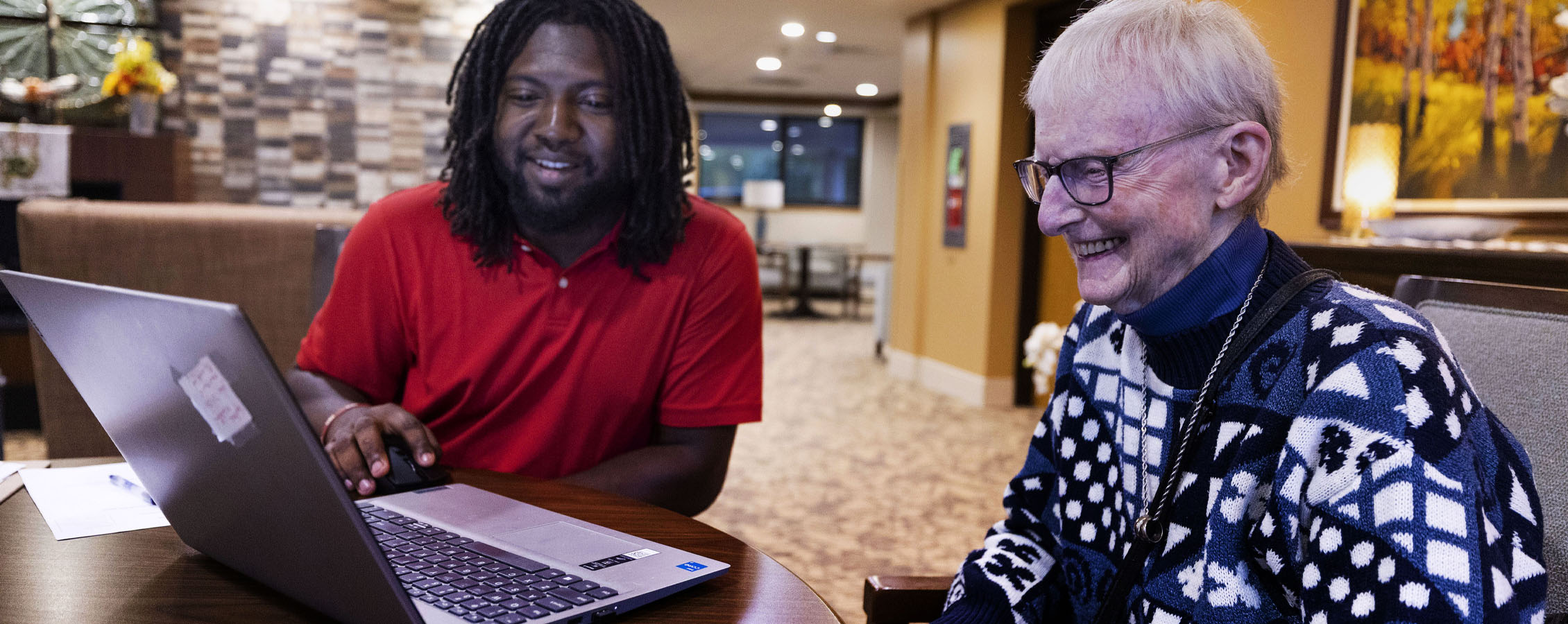A student and a senior citizen smile at a laptop screen together.