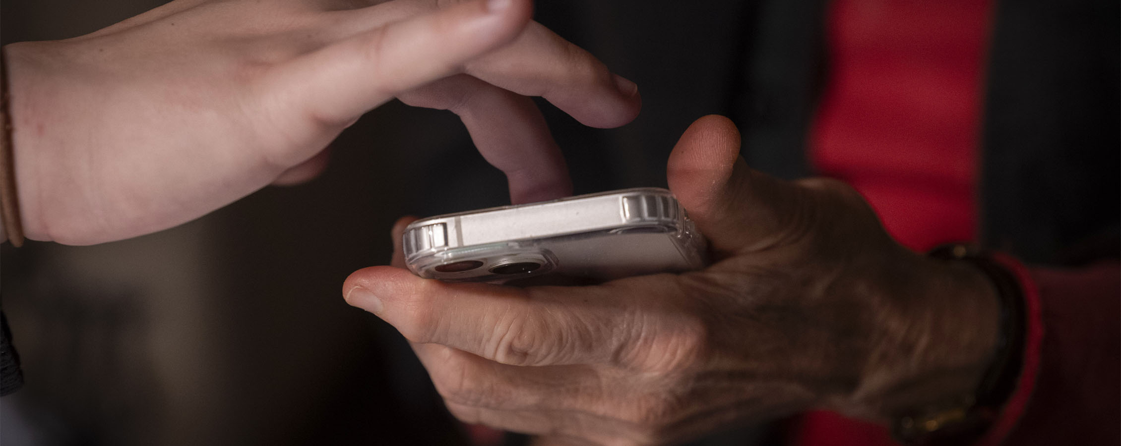 One person holds a phone while another person taps on its screen.
