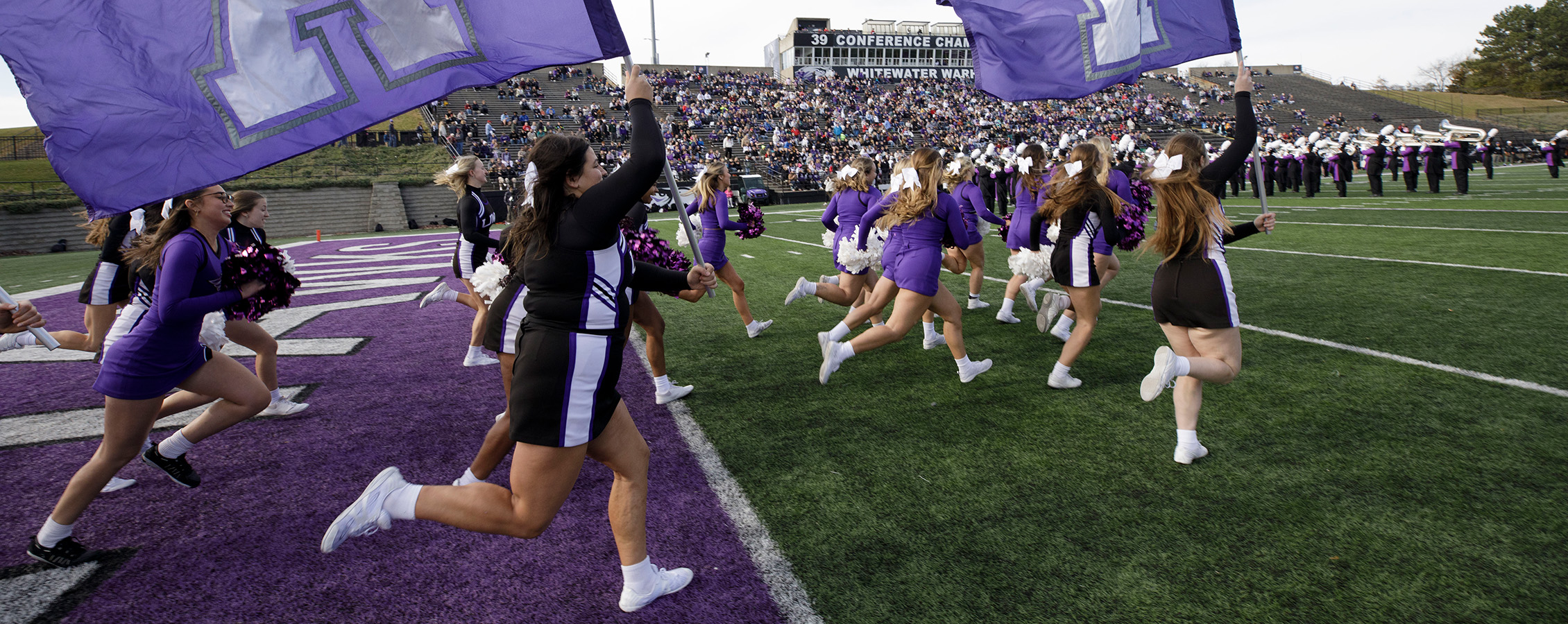 Cheerleaders run onto the field before a football game waving flags.