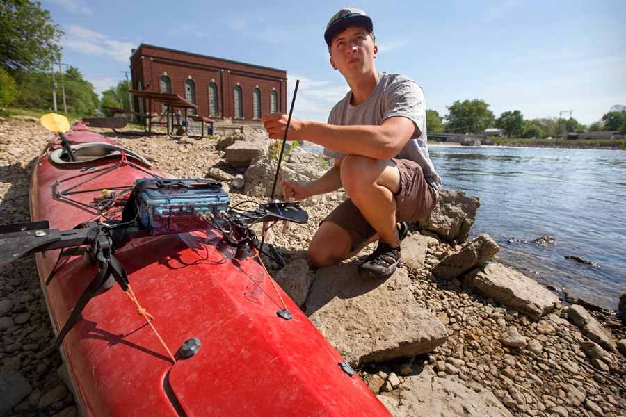 Image: Student kneeling next a conoe and a river
