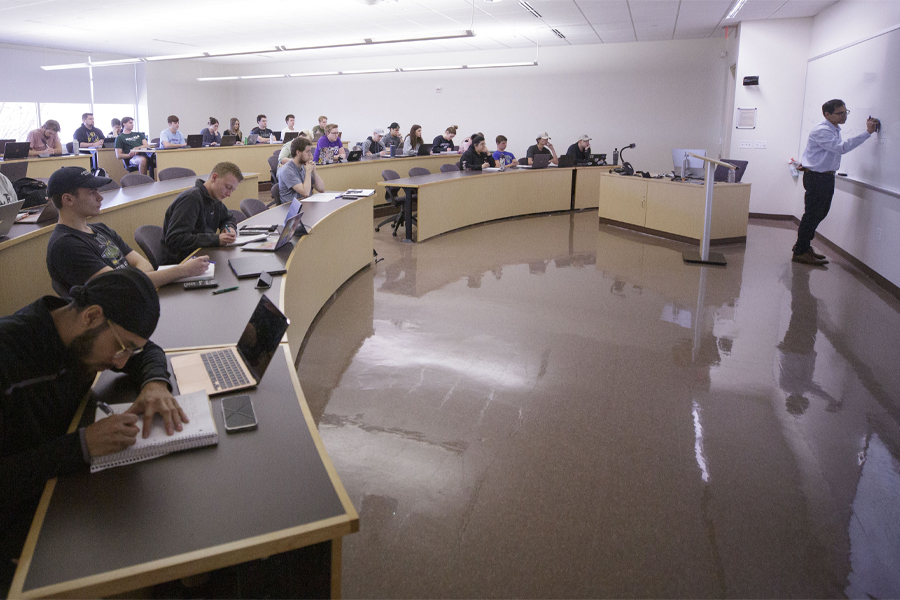 An instructor teaches at the front of a lecture hall filled with students.