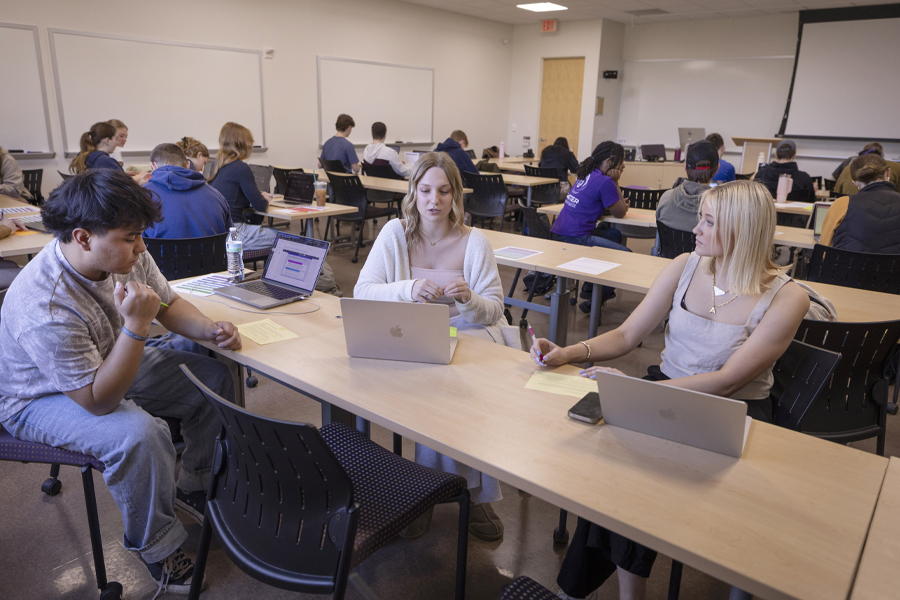 Three students work together on their laptops during class.