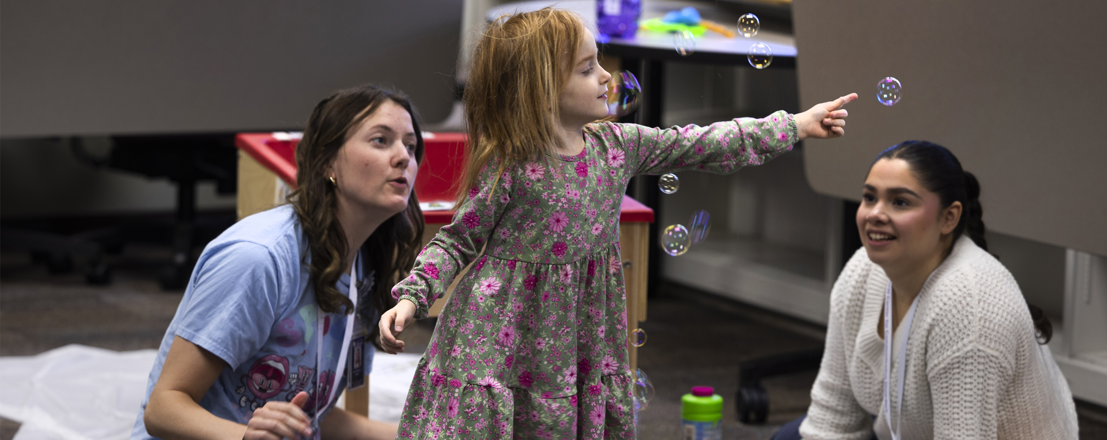 Young child pops bubbles as two students watch.