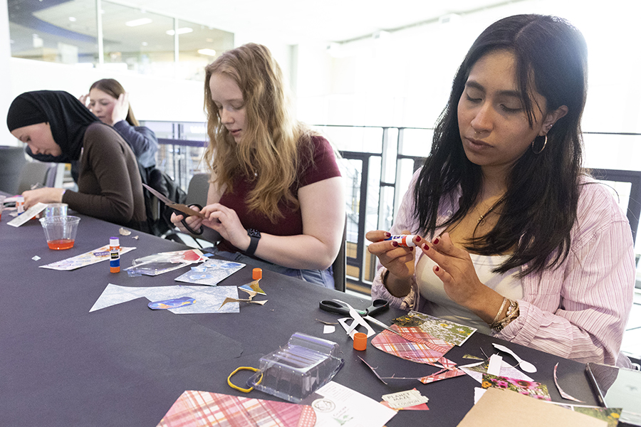 Three students sit at a table with a purple tablecloth and craft with scissors.