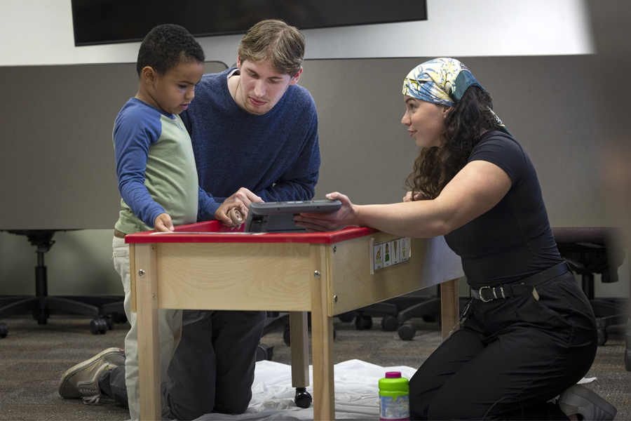 Two students use a tablet to play with a young child.