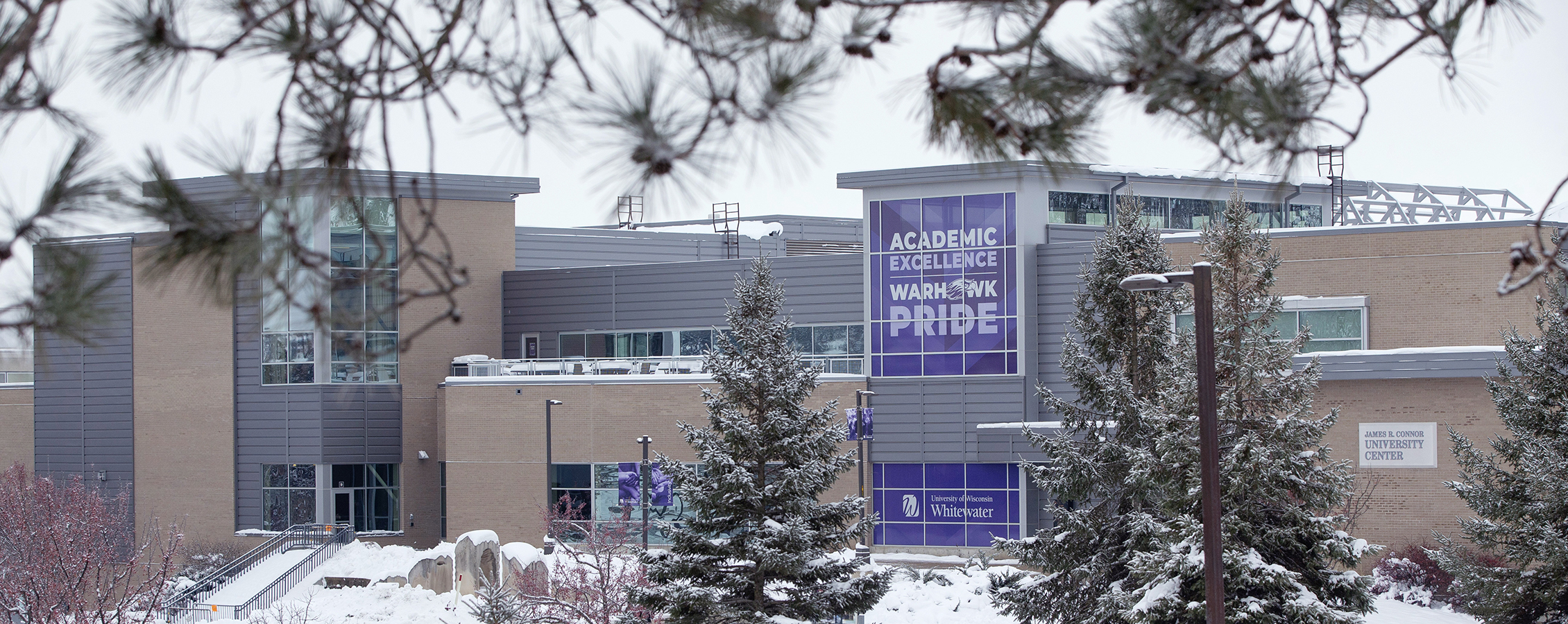 The University Center in winter shows a purple banner that says Academic Excellence and Warhawk Pride.