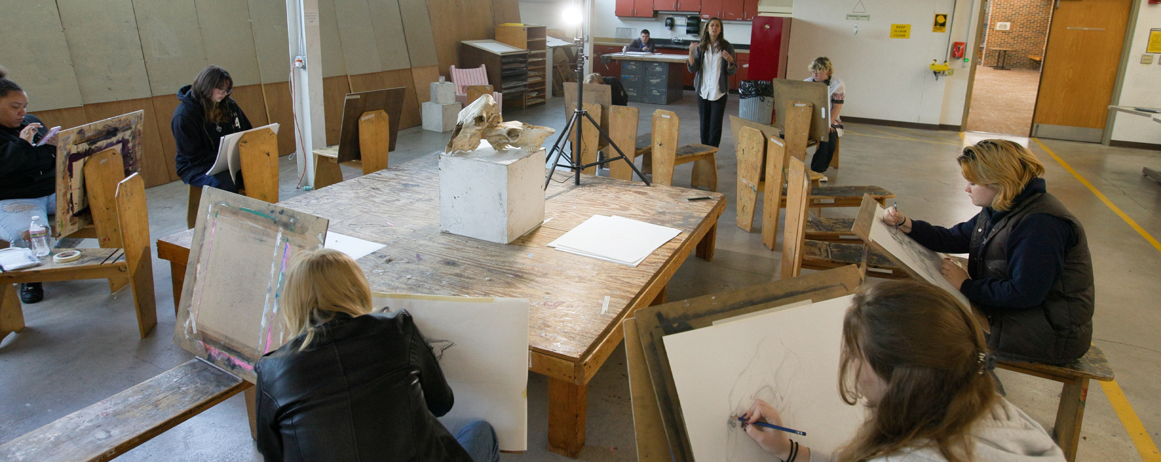 A classroom shot of students drawing on canvases.