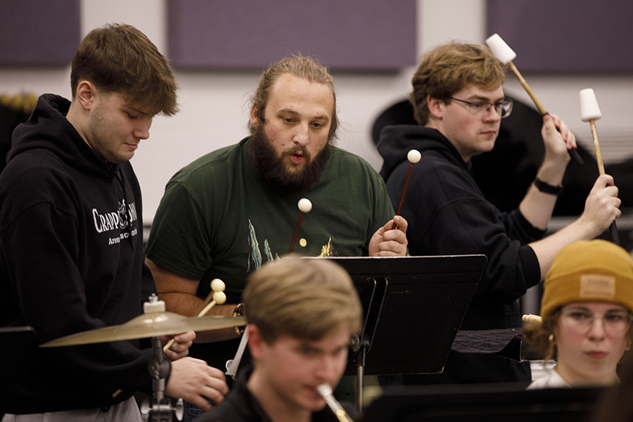 Three students stand together, reading music, playing percussion.