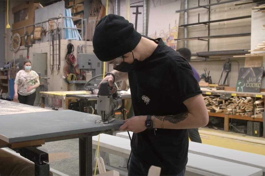 A student uses a drill to make backdrops for an upcoming opera.