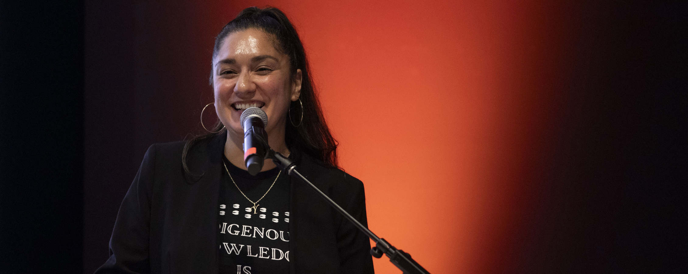 A person smiles as they speak into a microphone.