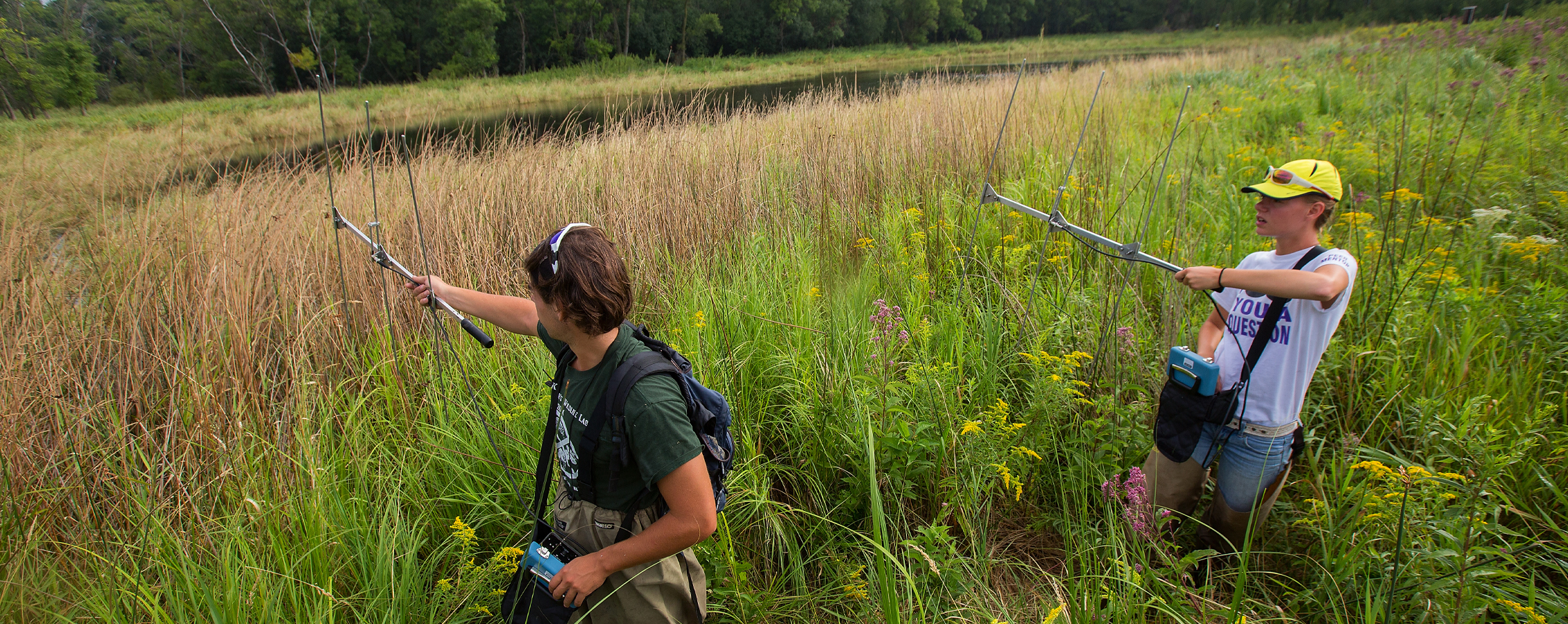 Two people walk through a field holding research devices.