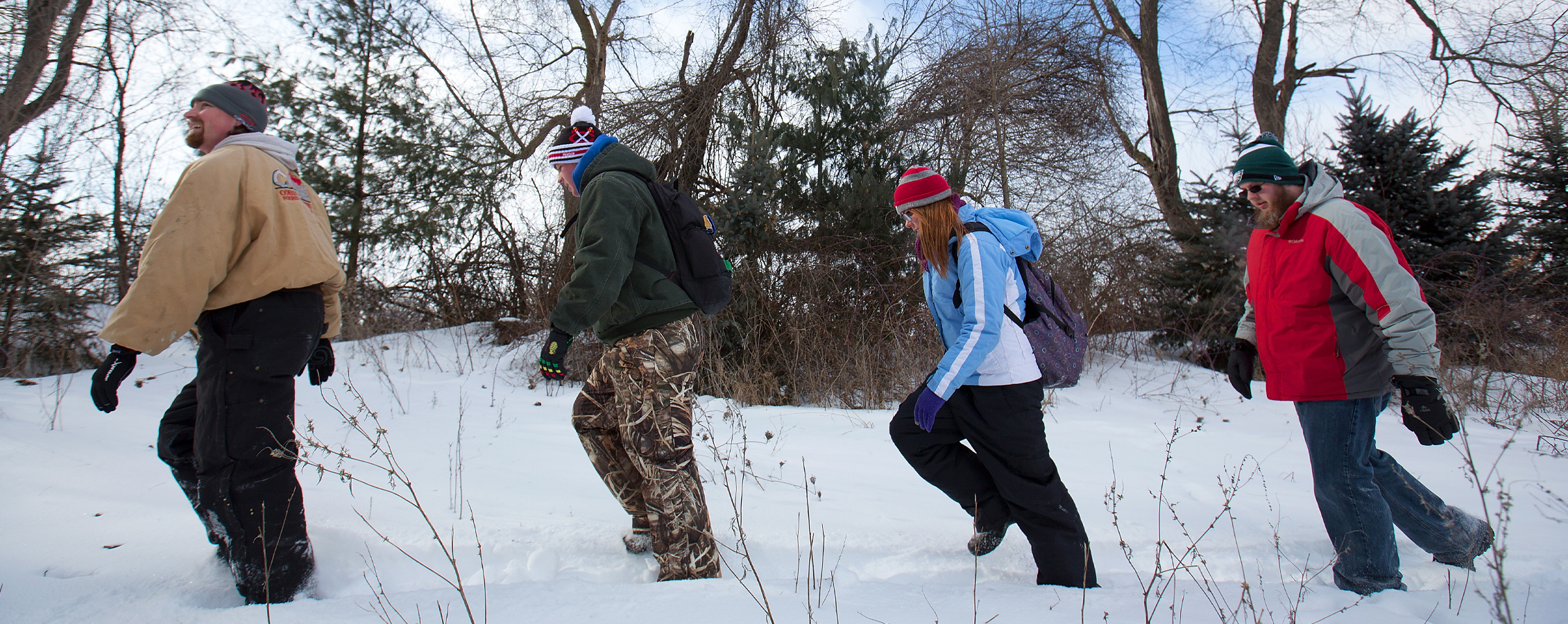 Four students walk through the snow in a wooded area.