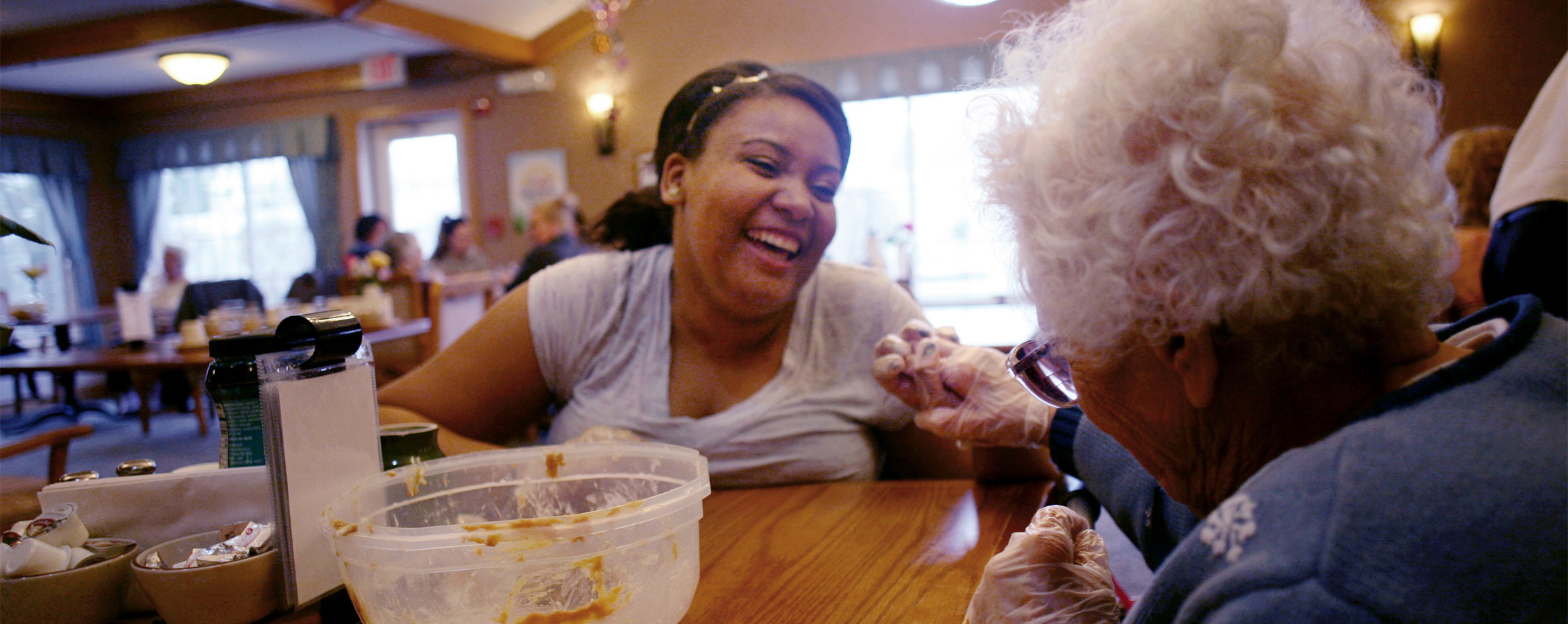 A student smiles and laughs with an elderly woman and holds her hand.