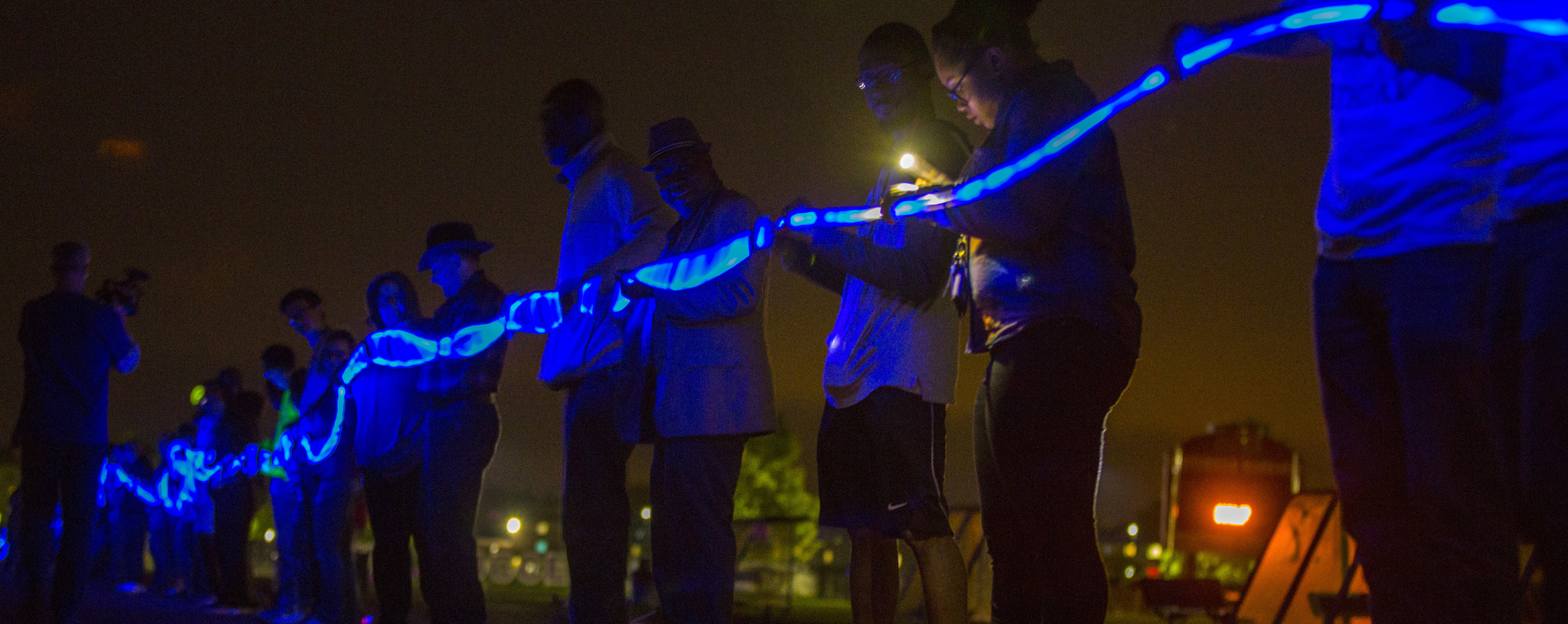 Students stand in a line outside holding a long blue glowstick.