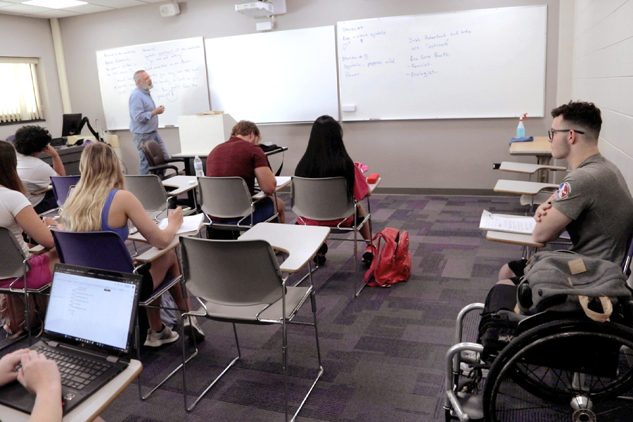 A lecturer stands in front of a white board.