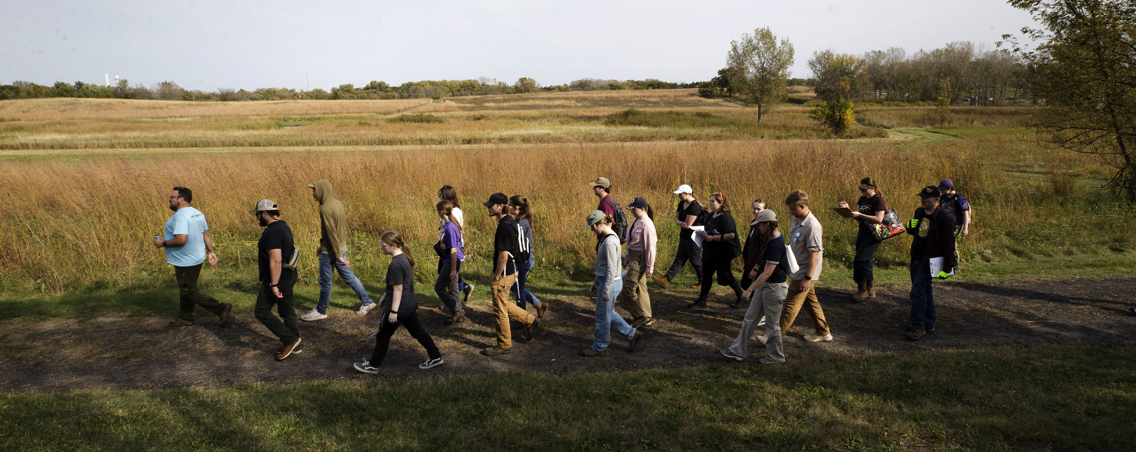 A class walks on a trail in the prairie.