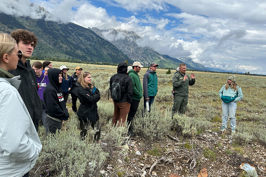 Tyler Brasington stands with students amidst mountains, fields, and puffy clouds.