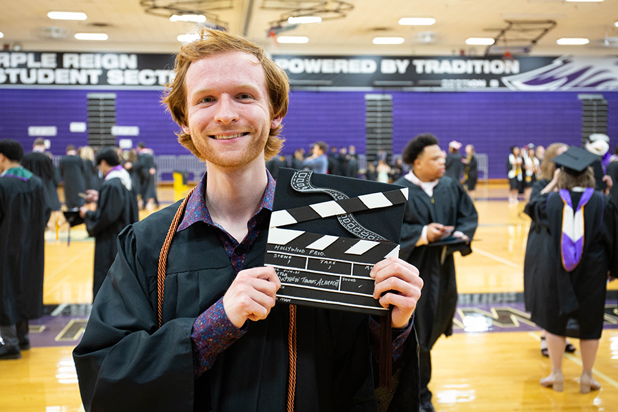 A student at graduation is dressed in academic regalia shows his cap decorated like a clapperboard.
