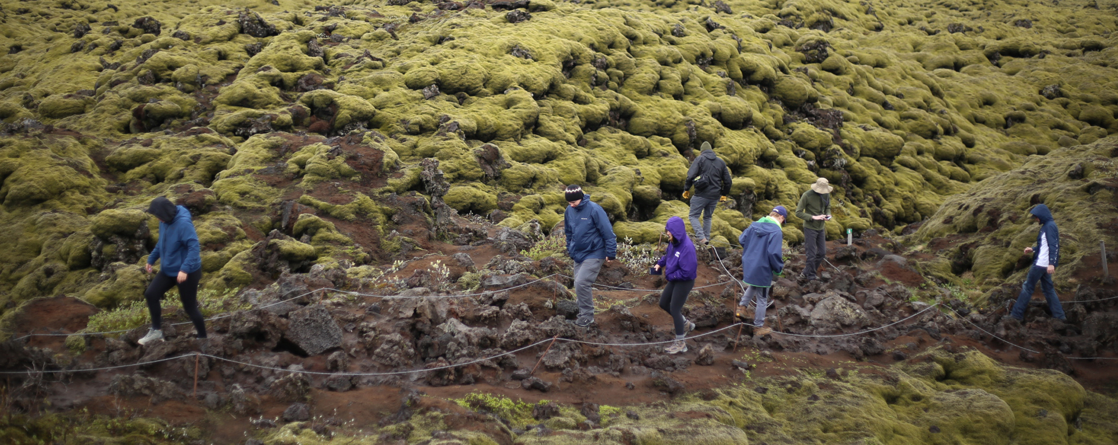 Students walk on a path of rugged terrain.