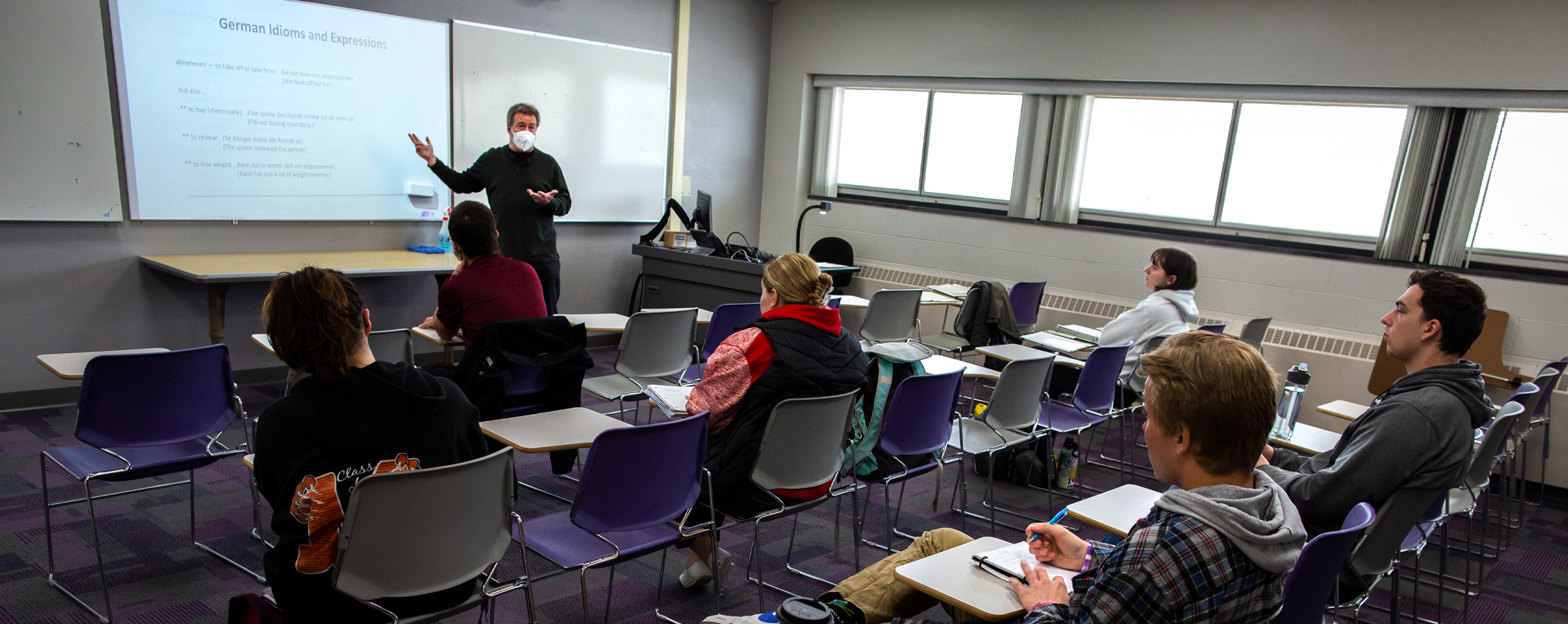 A German faculty member speaks by a whiteboard during class.