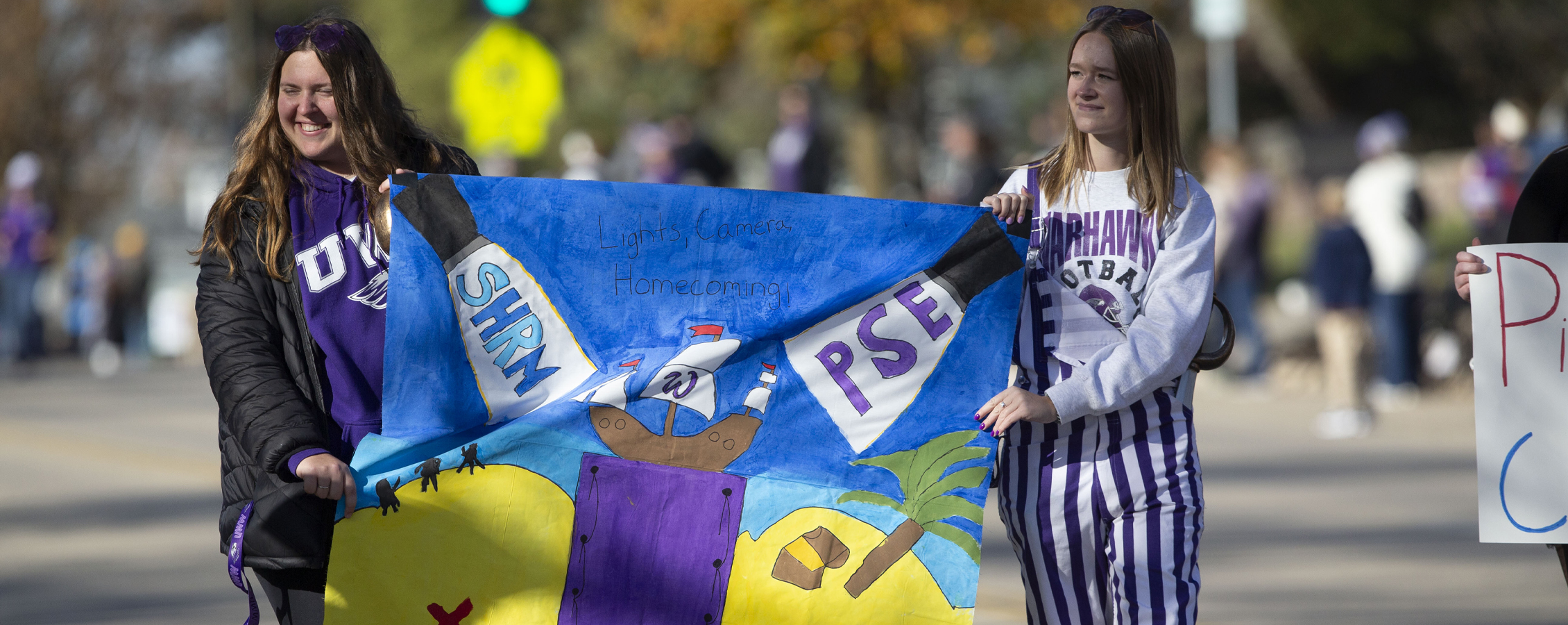 Two students walk in the Homecomig parade and hold a flag that says SHRM on one side and PSE on the other side.