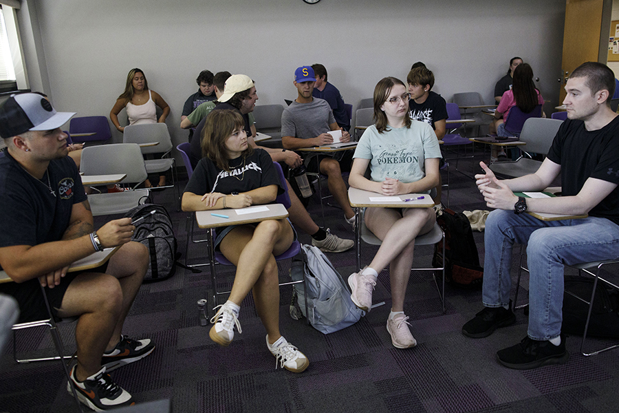 A group of four students push their desks together to have a discussion in a classroom.
