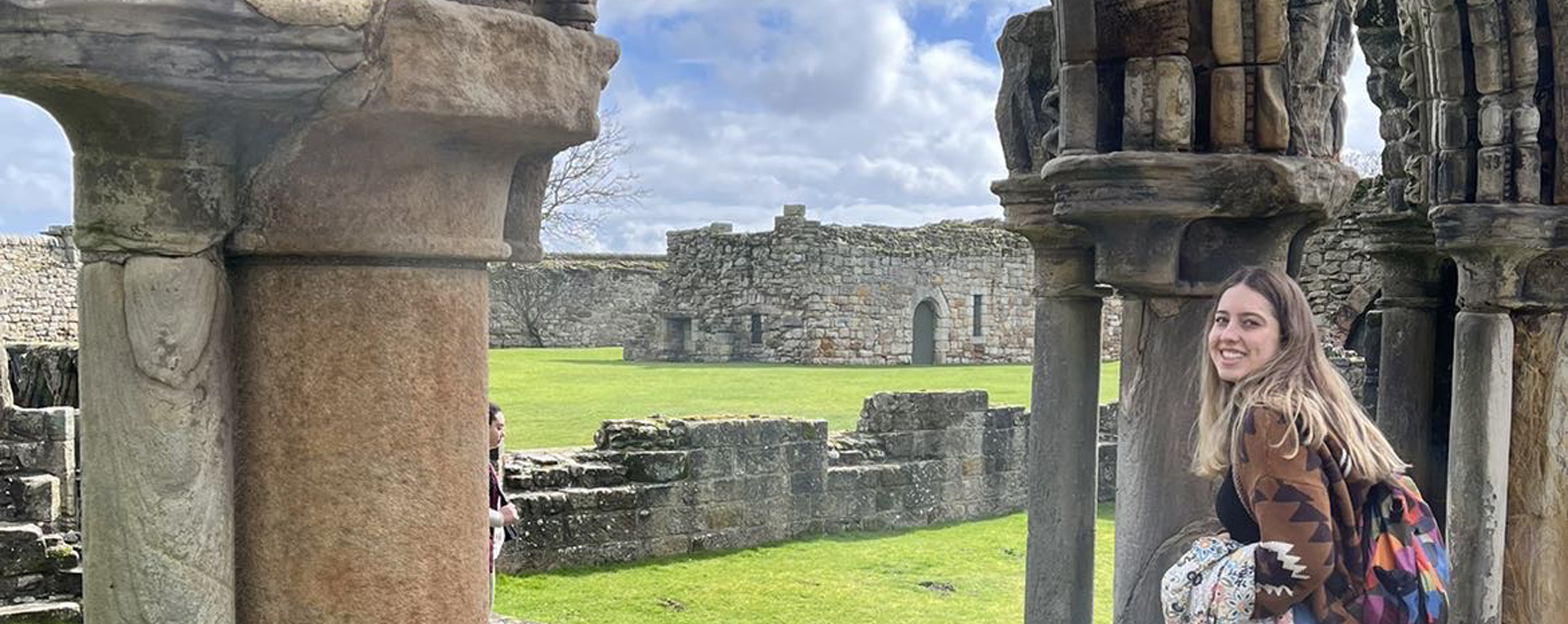 A student stands among the remains of stone architecture in Scotland.